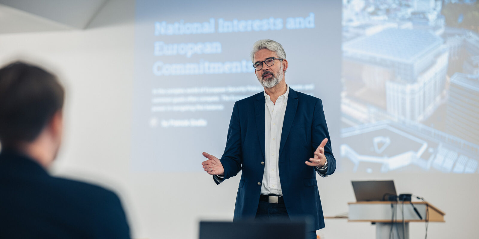 Professor Eckhard Schröter hält eine Vorlesung, im Hintergrund ist eine Bildschirmpräsentation zu sehen